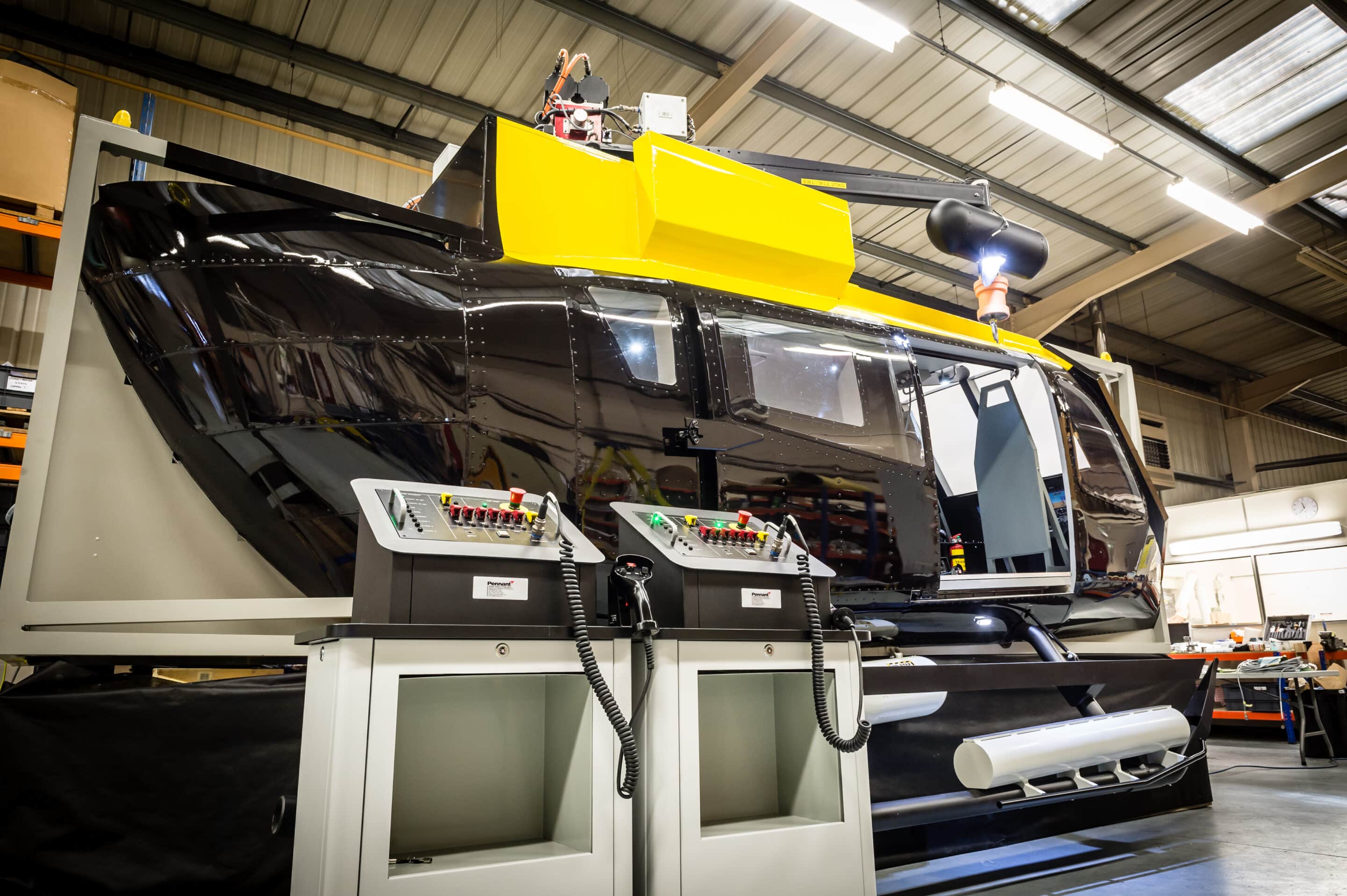 A train simulator sat in an industrial workshop. The simulator is black and yellow with numerous buttons.
