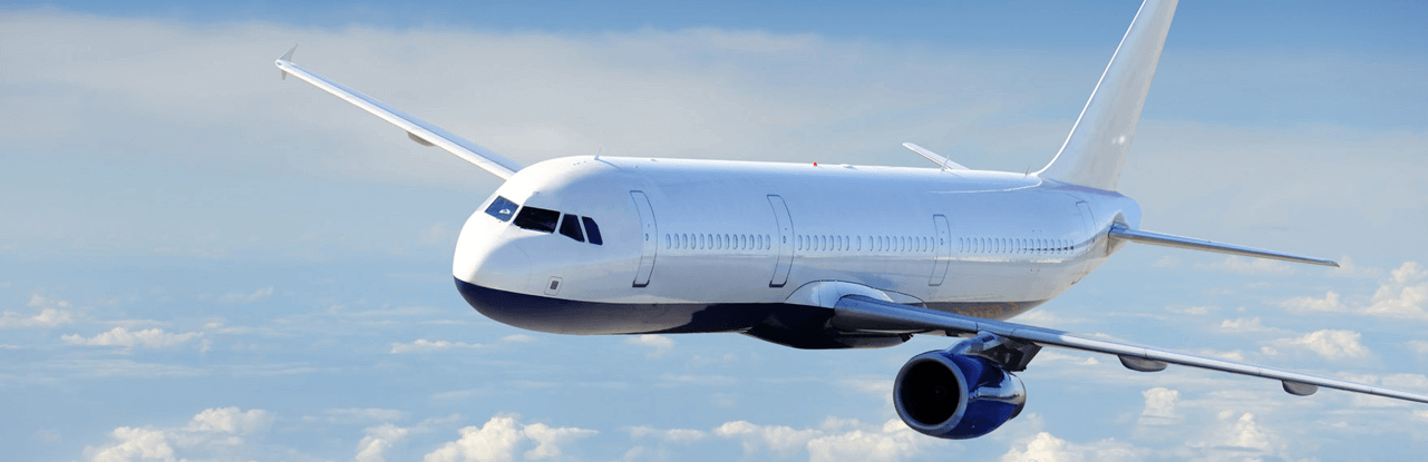 A white and blue plane flying through the sky. The sky is blue with faint white clouds.
