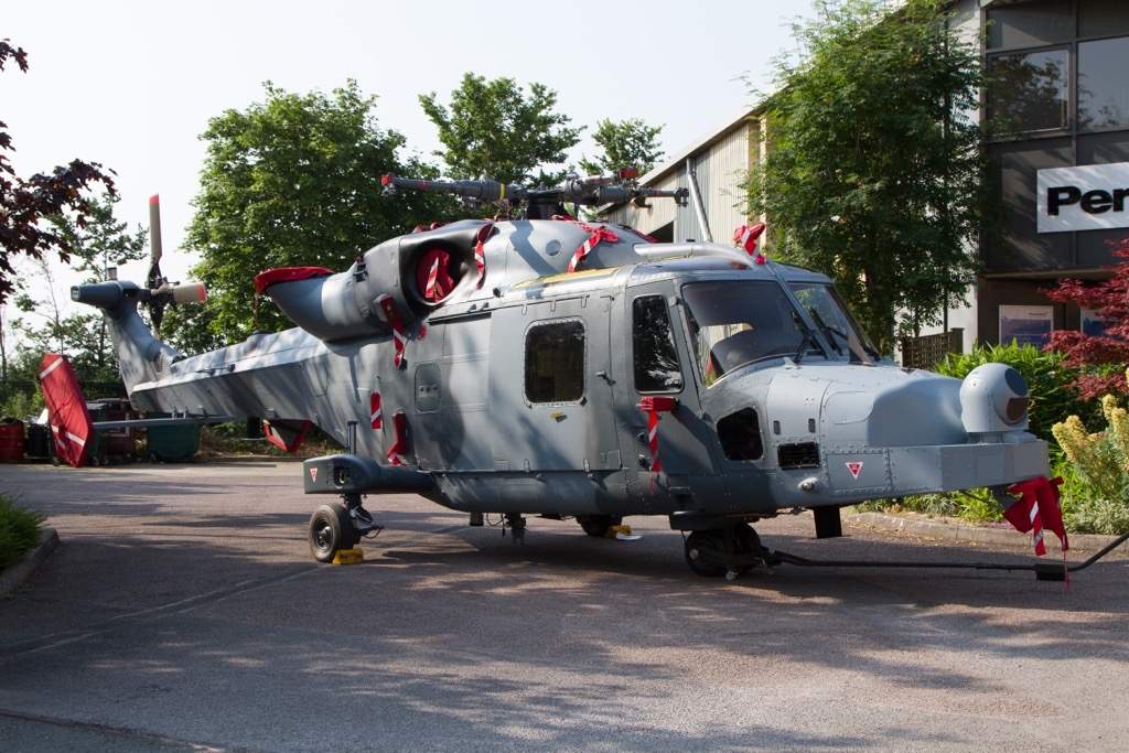 A grey defence helicopter sat outside an office building. The day appears to be nice weather